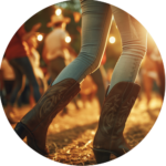 Close-up of a person's legs in cowboy boots dancing on a straw-covered ground, with a group of dancers in the background under warm, glowing lights.